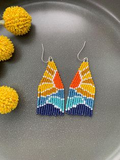 a pair of colorful beaded earrings sitting on top of a metal tray next to yellow flowers