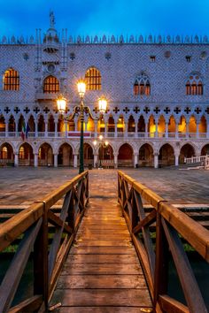 a wooden bridge leading to a large building with lights on it's sides at night