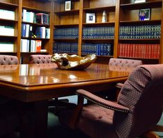 a large wooden table with chairs around it in front of bookshelves filled with books