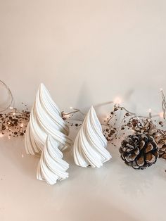 three white frosted christmas trees sitting on top of a table next to a pine cone