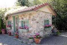 a small stone building with potted flowers on the front and side window sill