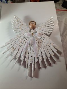 an angel made out of plastic and beads on a piece of white paper with gold accents