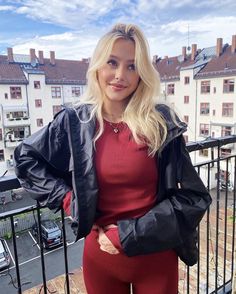 a woman in red is standing on a balcony with her arms crossed and looking at the camera