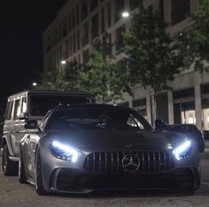 two cars parked next to each other on a street at night with buildings in the background