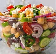 a salad in a glass bowl on a marble counter top, with tomatoes, cucumbers, onions and chickpeas