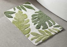 a bathroom rug with green leaves on it in front of a bathtub and toilet