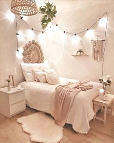 a white bedroom with lights strung from the ceiling and a bed covered in pink blankets