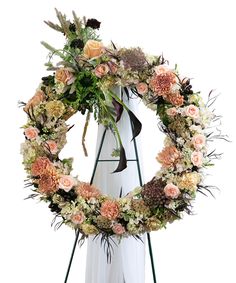 a wreath with flowers and greenery hanging on a white wall next to an easel