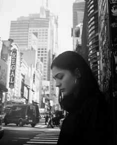 a woman standing in the middle of a street looking at her cell phone with city buildings in the background