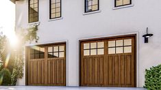 two brown garage doors are open in front of a white house with green bushes and trees