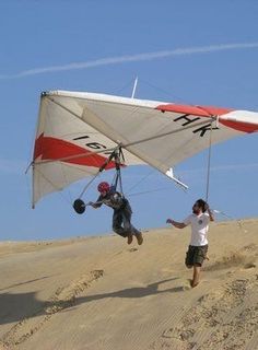 two people are flying a kite in the air on top of a sand dune hill