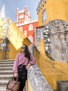 a woman in pink sweater and black skirt standing on steps with handbag near yellow building