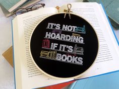 there is a cross stitch on top of an open book with the words it's not hoarding if it's books