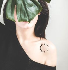 a woman with a tattoo on her shoulder holding a large green leaf in front of her face