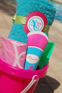 a pink pail filled with lots of items on top of a sidewalk next to a swimming pool