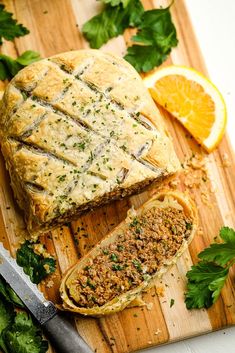 a cutting board topped with meat and bread next to sliced oranges on top of it