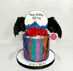 a birthday cake decorated with books and a dragon's wings is shown in front of a white background