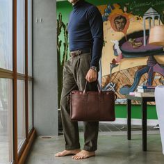 a man holding a brown briefcase standing next to a window