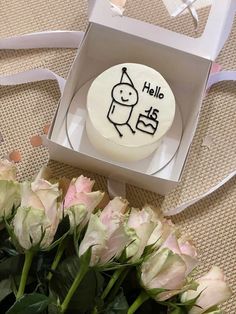 there is a cake in the box with flowers on the table next to it that says hello