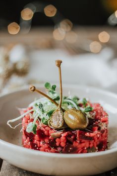 a white plate topped with red rice covered in veggies and an olive on top