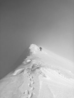 a person walking up the side of a snow covered mountain with footprints in the snow