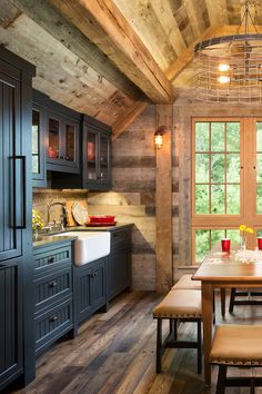 a kitchen with wooden walls and flooring next to a dining table in front of a window