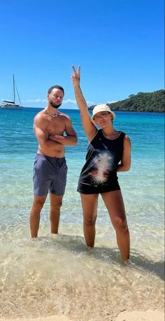 a man and woman standing in shallow water at the beach with their arms up to the sky