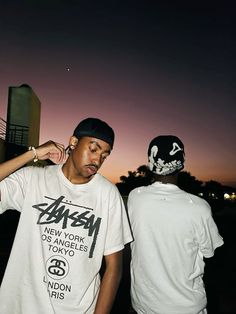 two young men standing next to each other in front of a city at night time