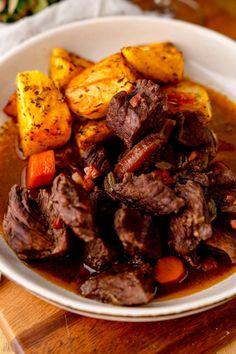 a white bowl filled with meat and vegetables on top of a wooden table next to a fork