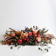 an arrangement of flowers and greenery on a white surface