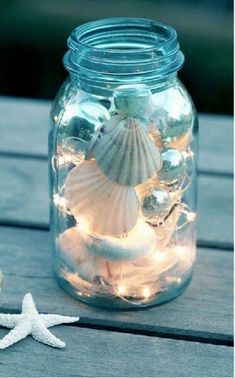 a jar filled with sea shells and lights on top of a wooden table next to a starfish