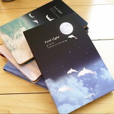 three notebooks sitting on top of each other with pictures of dolphins flying in the sky