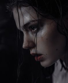 a woman with black hair and white makeup looks into the distance while she's covered in water