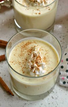 two glasses filled with dessert sitting on top of a white table next to cinnamon sticks