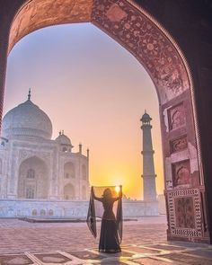 a woman standing in front of an archway with the sun setting behind her and looking at the tajwa