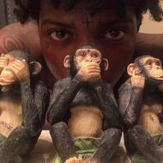 a woman looking at three monkey figurines in front of her face, with one holding the other