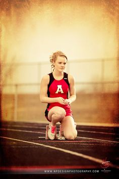 a woman kneeling down on top of a track wearing a red shirt and black shorts