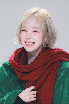 a woman with blonde hair wearing a red scarf and green jacket smiling at the camera