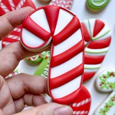 a hand holding a candy cane cookie in front of christmas cookies on a white surface