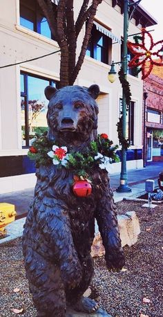 a statue of a bear with flowers in its mouth on the side of a street