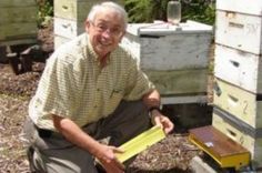 an old man kneeling down next to some beehives