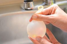 a person holding an object in their hand near a sink faucet and soap dispenser