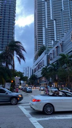 cars are driving down the street in front of tall buildings and palm trees at dusk