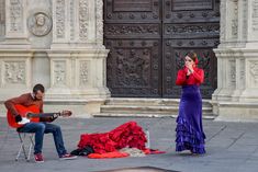 a man and woman sitting on the ground playing guitar in front of an ornate building