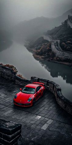 a red sports car parked on the side of a road next to a body of water