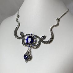 This Medusa inspired necklace is made with a large antiqued silver plated double snake motif, filigrees and findings. Sparkling glass crystals in DARK SAPPHIRE BLUE accent the eyes and centerpiece.Snakes are 3 5/8" across with a total height of approximately 4 inches from snake tale to bottom of pendant drop. The very center jeweled portion is 2 1/4" tall. Necklace is adjustable 15-18" with a lobster clasp and chain extender in the back. If you would like a different length or stone color, pleas Snake Motif, Fantasy Jewellery, Medusa Snake, Antique Silver Necklace, Dark Sapphire, Blue Accent, Choker Pendant, Inspired Necklace, Expensive Jewelry