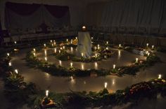 a circular arrangement of candles in the middle of a room filled with wreaths and flowers