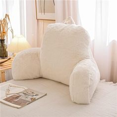 a large white pillow sitting on top of a bed next to a book and lamp