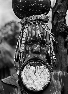 a man with an odd face and headpieces on his head is standing in front of a tree