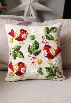 a white pillow with flowers and birds on it sitting on a couch next to a christmas tree